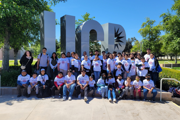  Students and families from Synergy Academies pose for a large group photo in front of a university sign during Family University Visit day.
